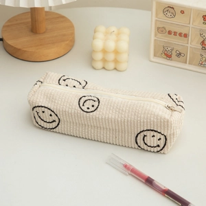 Close-up of off-white corduroy pencil case with smiley face embroidery on a wooden desk