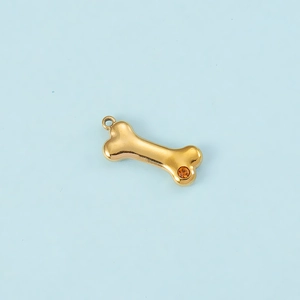 Macro shot of gold dog bone pendant with orange zircon inlay on light blue background