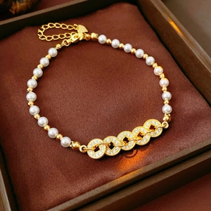 Detail of white pearl bracelet with gold beads and zircon rings on brown velvet