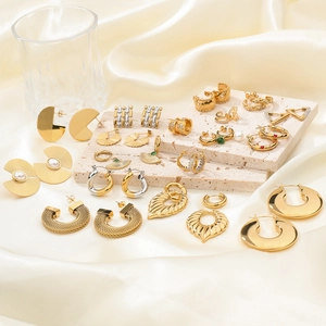 Detailed collection of gold plated hoop earrings and pearl studs on beige stone