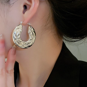 Detail view of large silver hoop earrings with quilted star texture on a model's ear