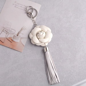 Close-up of white PU leather camellia keychain with tassel and silver hardware clasp
