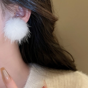 Close-up of a model wearing a white fluffy faux fur ball earring for winter outfits