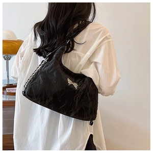 Detail of black pleated bucket bag featuring a silver butterfly and metal chain strap