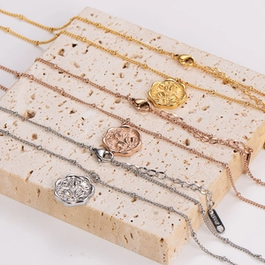 Three dainty cherry blossom necklaces in gold, silver and rose gold on a stone base