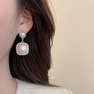 Detail of square pearl earrings with diamond accents worn by a model in warm light