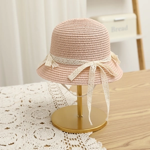 Detail of pink straw hat with lace bow and windproof cord on a golden metal stand