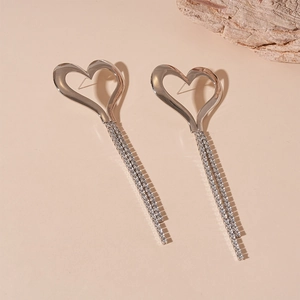 Macro view of silver heart earrings with long rhinestone tassels on a beige background