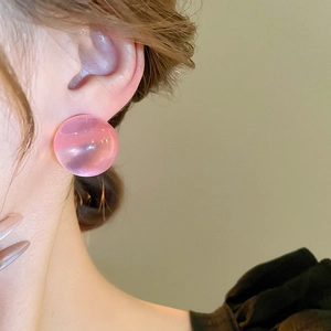 Gros plan de boucles d'oreilles sphères en résine rose translucide portées par un mannequin