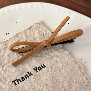 Detailed view of a brown velvet bow hair clip on a decorative card in a white ceramic dish
