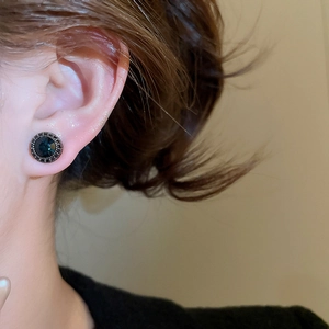 Close-up of a vintage dark blue zircon stud earring on a model's ear with halo stones
