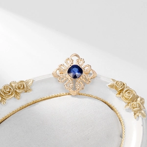 Elegant vintage gold brooch with a deep blue square gemstone on a white floral relief