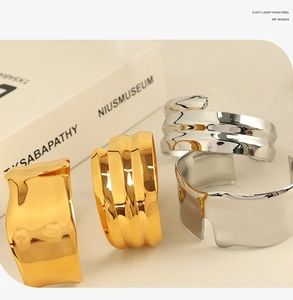 Artistic gold and silver wide bangles with irregular textures shown on beige background