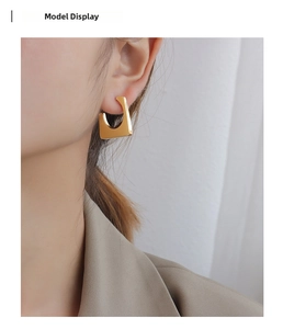 Profile view of a gold geometric trapezoid earring worn by a model in a tan suit