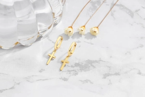 Detail of gold cross hoop earrings on white marble with elegant floral accents