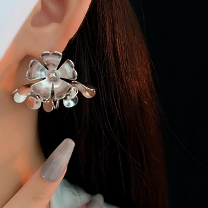 Close-up of minimalist silver metallic flower earrings worn by a model in deep lighting