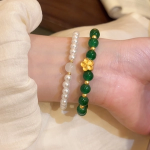 Primer plano de elegantes pulseras de piedra verde y perlas con flor dorada