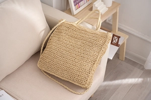 Detail of hand-woven straw tote bag with round handles and long strap on a soft beige sofa