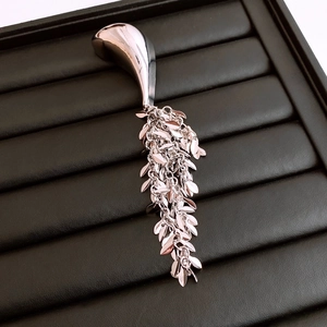 Detailed close-up of silver geometric tassel brooch with cascading leaf chains on black leather