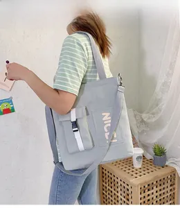 Detail of light green canvas tote bag with buckle pocket and letters in indoor setting