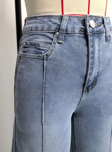 Detail van de lichtblauwe high-waist jeans met middennaad en metalen klinknagelaccenten