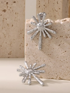 Macro shot of silver sunflower earrings with lava texture on beige travertine stone