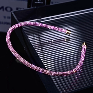Macro view of pink rhinestone headband with gold metal ends on black tray