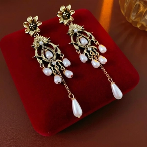 Vintage gold floral earrings with pearls and long tassels on a red velvet display