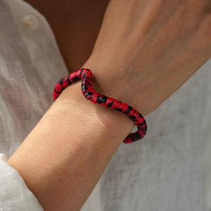 Detail of red and black striped wavy cuff bracelet with textured fiber on model wrist