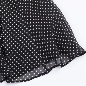Vista dettagliata del tessuto in chiffon nero leggero a pois bianchi con orlo drappeggiato