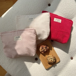Close-up of three corduroy makeup bags in pink, beige, and red on a cozy wool background