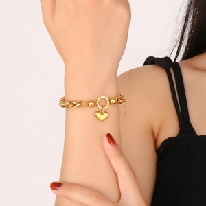 Detail of gold heart pendant chain bracelet on model wrist with polished metallic finish