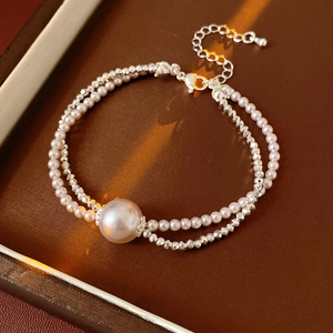 Detailed view of double-layer pearl and silver bead bracelet on a brown jewelry box
