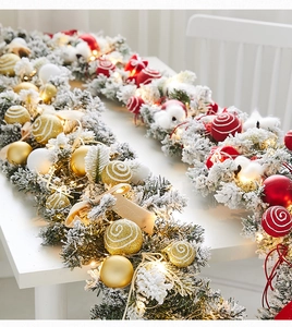 Close-up of white flocked Christmas garland with gold balls, red swirls and warm LED lights