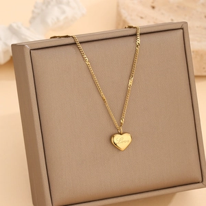 Elegant gold heart necklace with Love engraving draped over a brown jewelry gift box