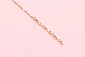 Macro detail of the golden stainless steel O-link chain on a soft pink background