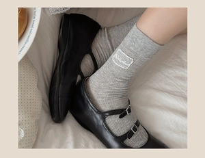 Close-up of grey ribbed mid-calf socks with heart label and black Mary Jane shoes