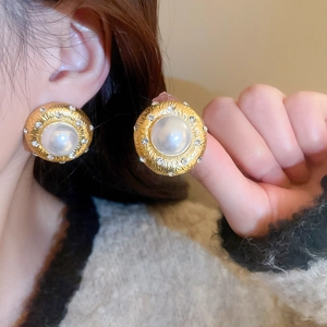 Close-up of vintage gold stud earrings with white faux pearl and rhinestone halo on model