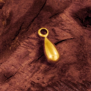Macro detail of high-polish gold teardrop pendant with smooth surface on wood