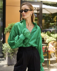 Detailed texture of emerald green satin shirt showing soft glossy fabric and elegant sleeves