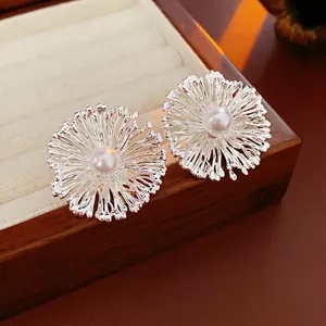 Silver flower stud earrings with central pearl accents on a wooden display box