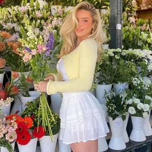 Detail of light yellow knit cardigan paired with tiered white lace mini skirt in floral setting
