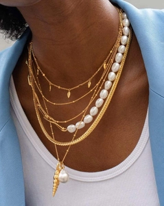 Close-up of triple-layered gold ocean necklaces with pearls on a blue blazer model