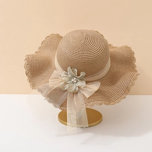 Détail d'un chapeau en paille avec nœud voilé, fleur et perles sur un support doré