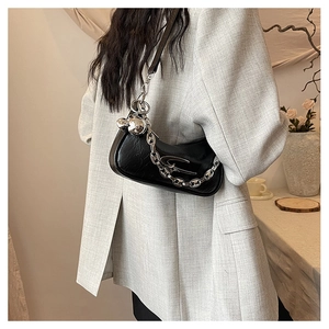 Close-up of black glossy crescent underarm bag with silver chain and star logo on a blazer