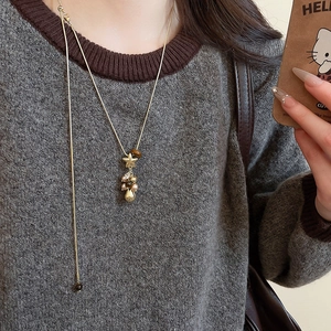 Détail du collier doré en Y avec breloques étoiles et perles porté sur un pull-over gris