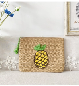 Detail of straw woven clutch featuring yellow and green pineapple embroidery and tassel