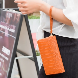 Detail of bright orange long wallet with crocodile texture and detachable wrist strap