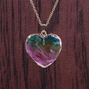 Close-up of rainbow crystal heart pendant with gold chain on dark wood background