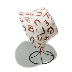 Dettaglio del cappello a secchiello in tela crema con motivi di cuori e lettere marroni